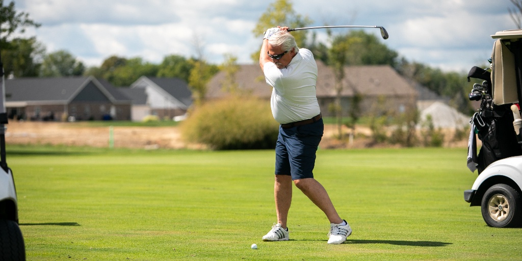 A man swings a club at a golf ball.