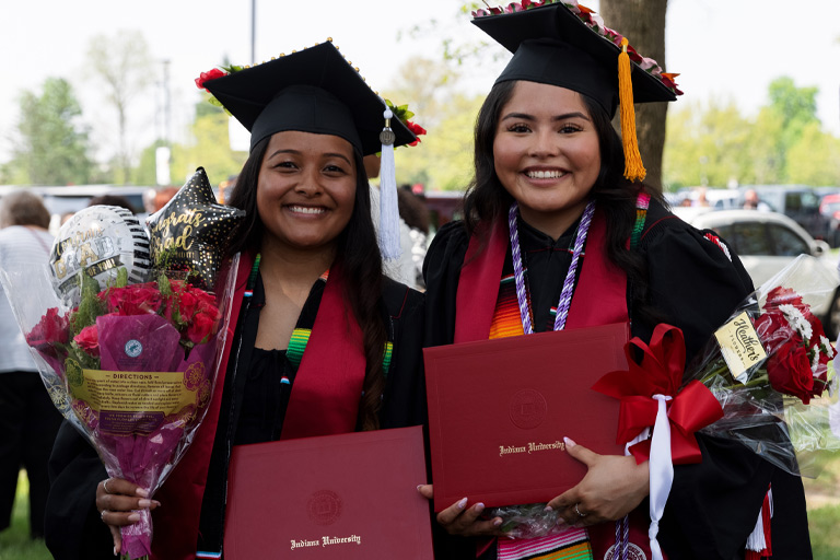 Two friends pose for a snapped pic with their diplomas and bundles of flowers