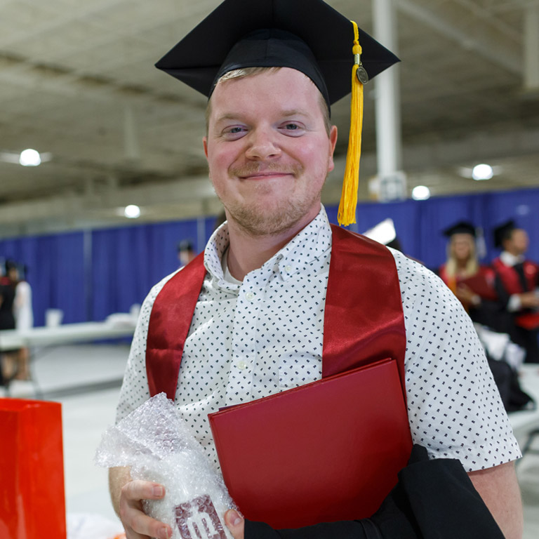A cheerful young graduate holds his IUK swag