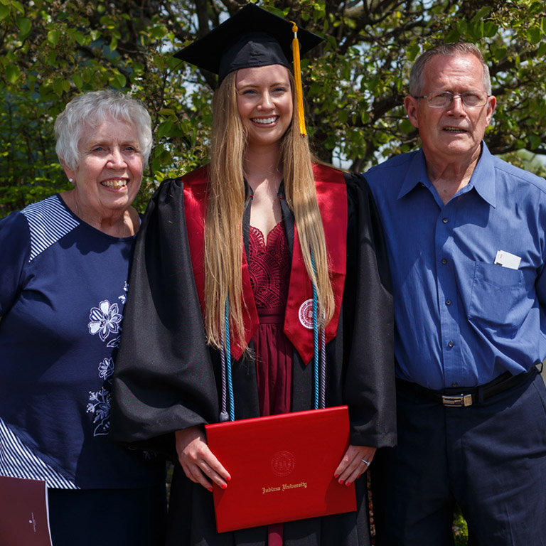 A senior couple in color-coordinated navy blue outfits snap a photo with their IUK graduate