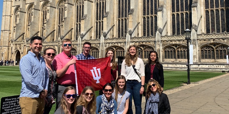 Students standing in front of a building holding an IU banner.